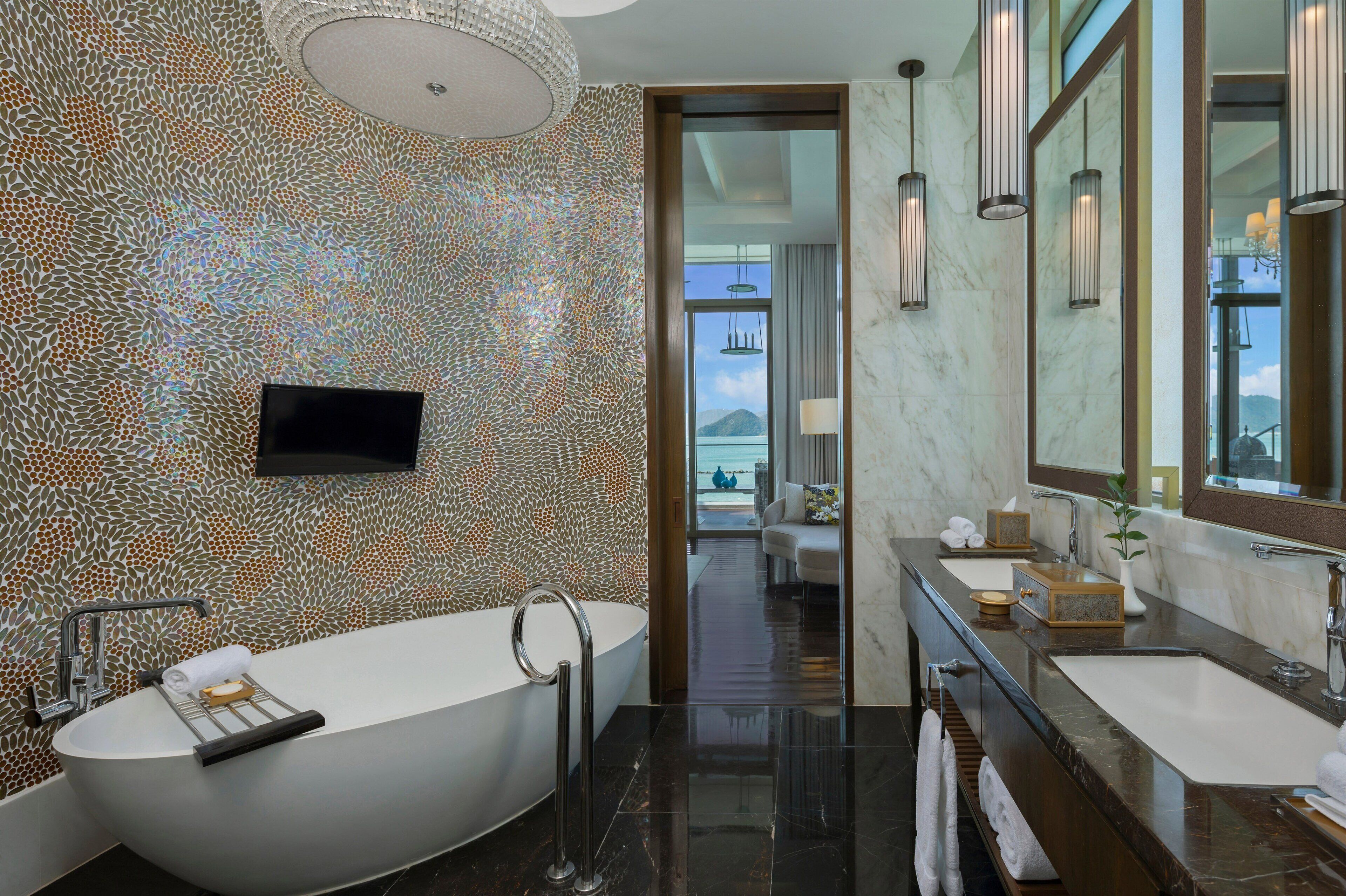 A modern bathroom with a freestanding bathtub, two sinks, a large mirror, and a television.