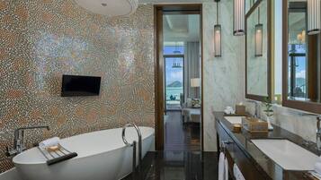 A modern bathroom with a freestanding bathtub, two sinks, a large mirror, and a television.