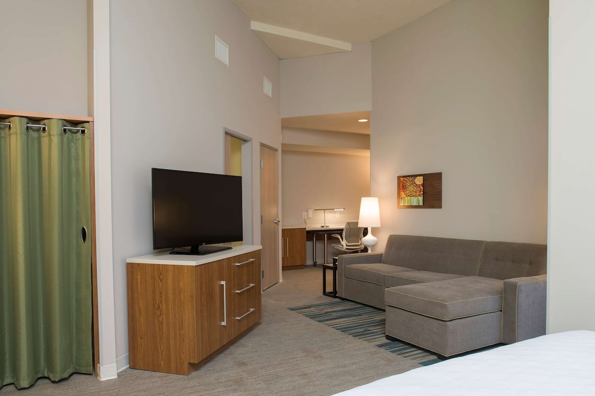 A hotel room with a TV, a sofa, a desk, and a lamp.