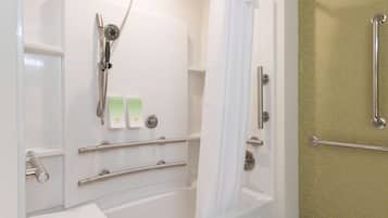 A bathroom with a bathtub, shower, and grab bars. There are two bottles of shampoo and a towel on the wall.