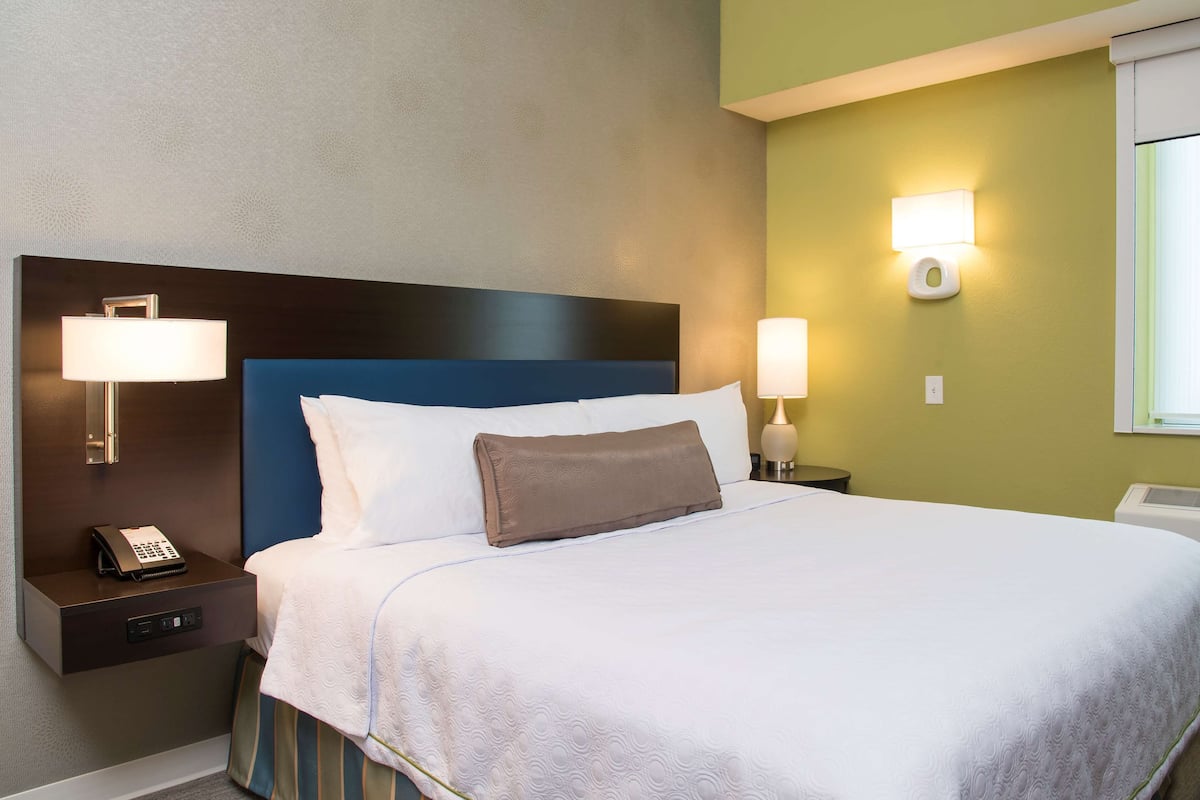 A neatly made bed with a blue headboard, two bedside lamps, and a nightstand with a phone.