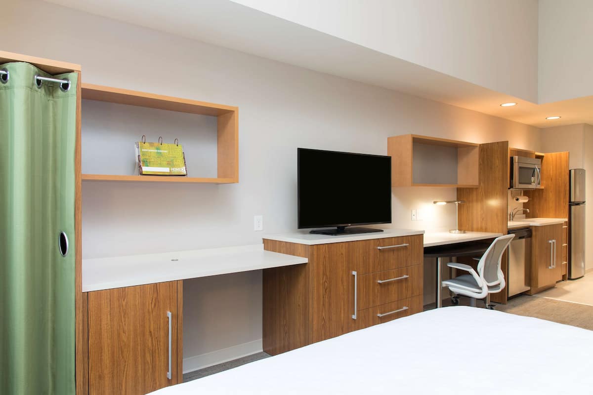A modern kitchen with wooden cabinets, a flat-screen TV, a microwave, and a refrigerator.