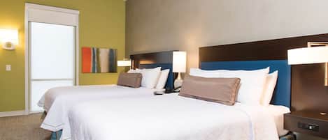 A hotel room with two beds, a door, and a wall-mounted lamp.