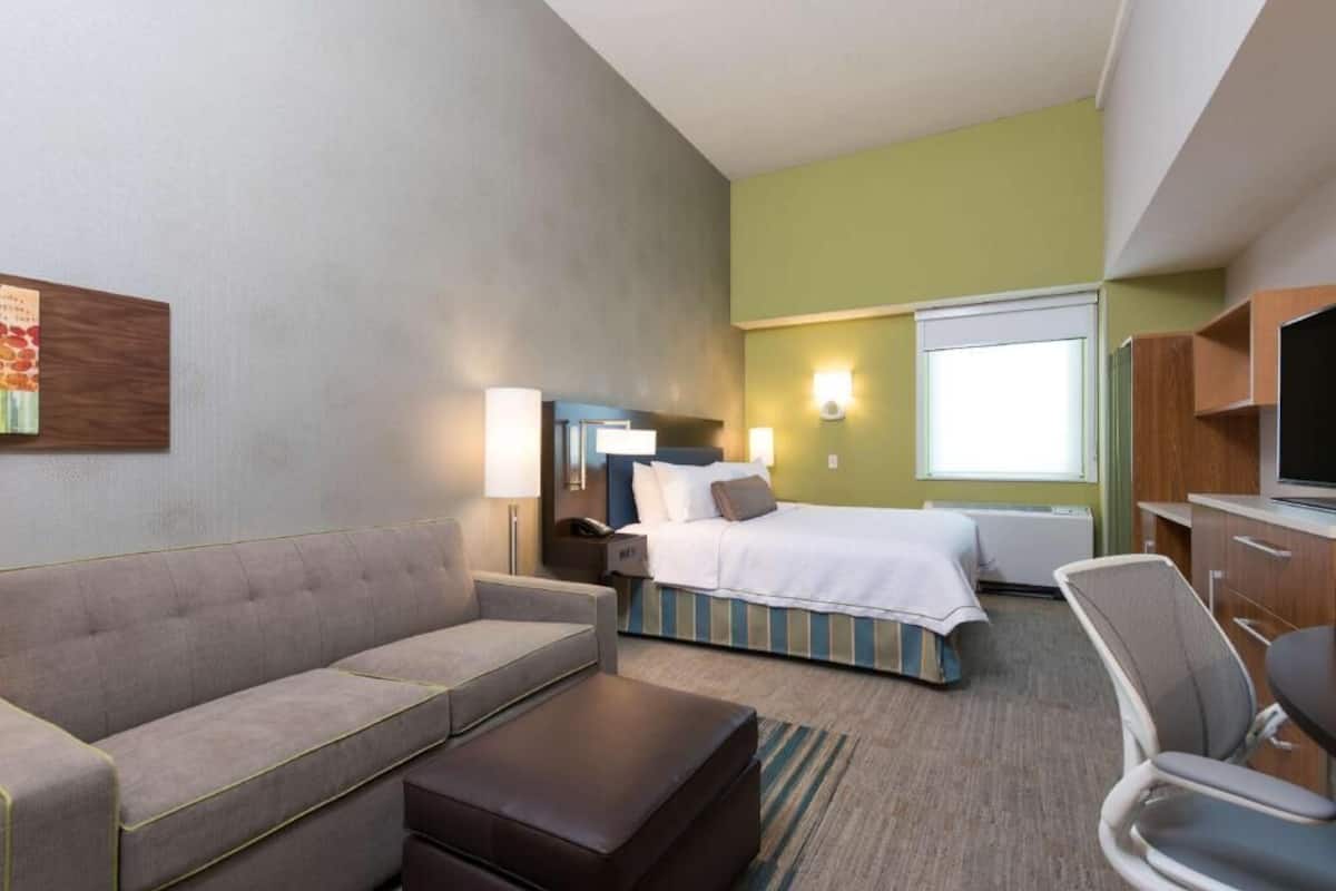A hotel room with a sofa, a bed, a desk, and a television.