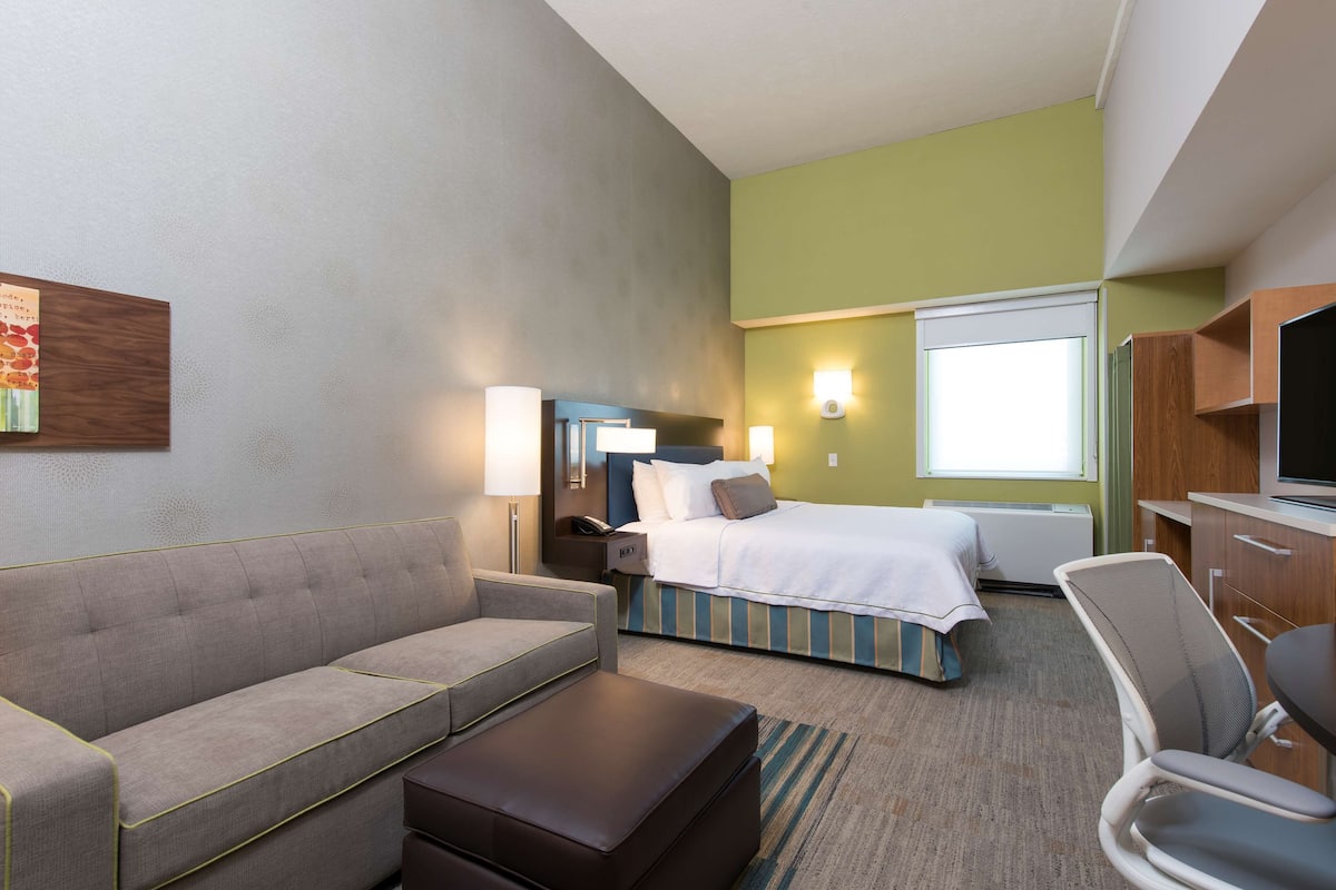 A hotel room with a bed, a sofa, a desk, and a TV.