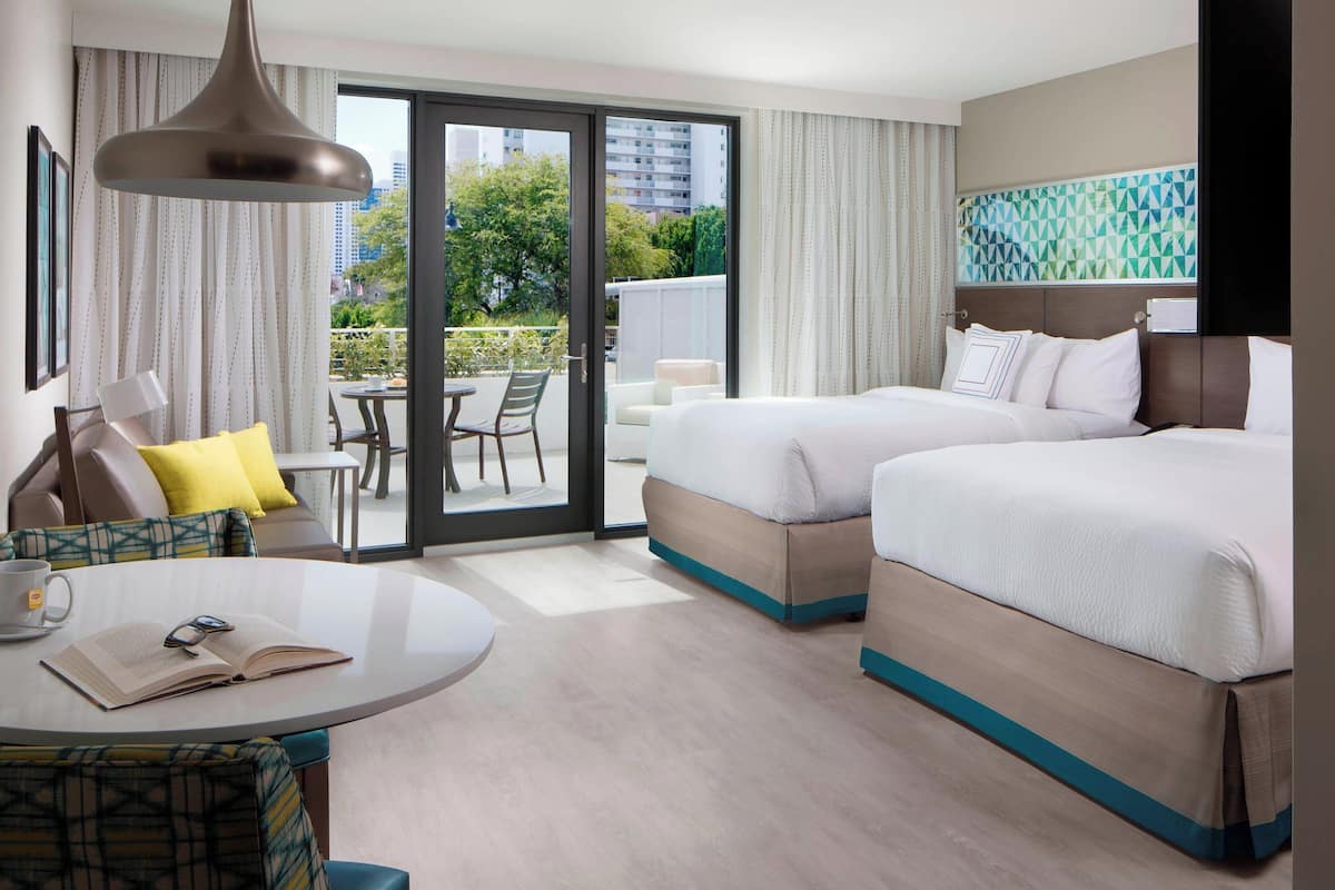 A hotel room with two beds, a balcony with a table and chairs, and a view of the city.