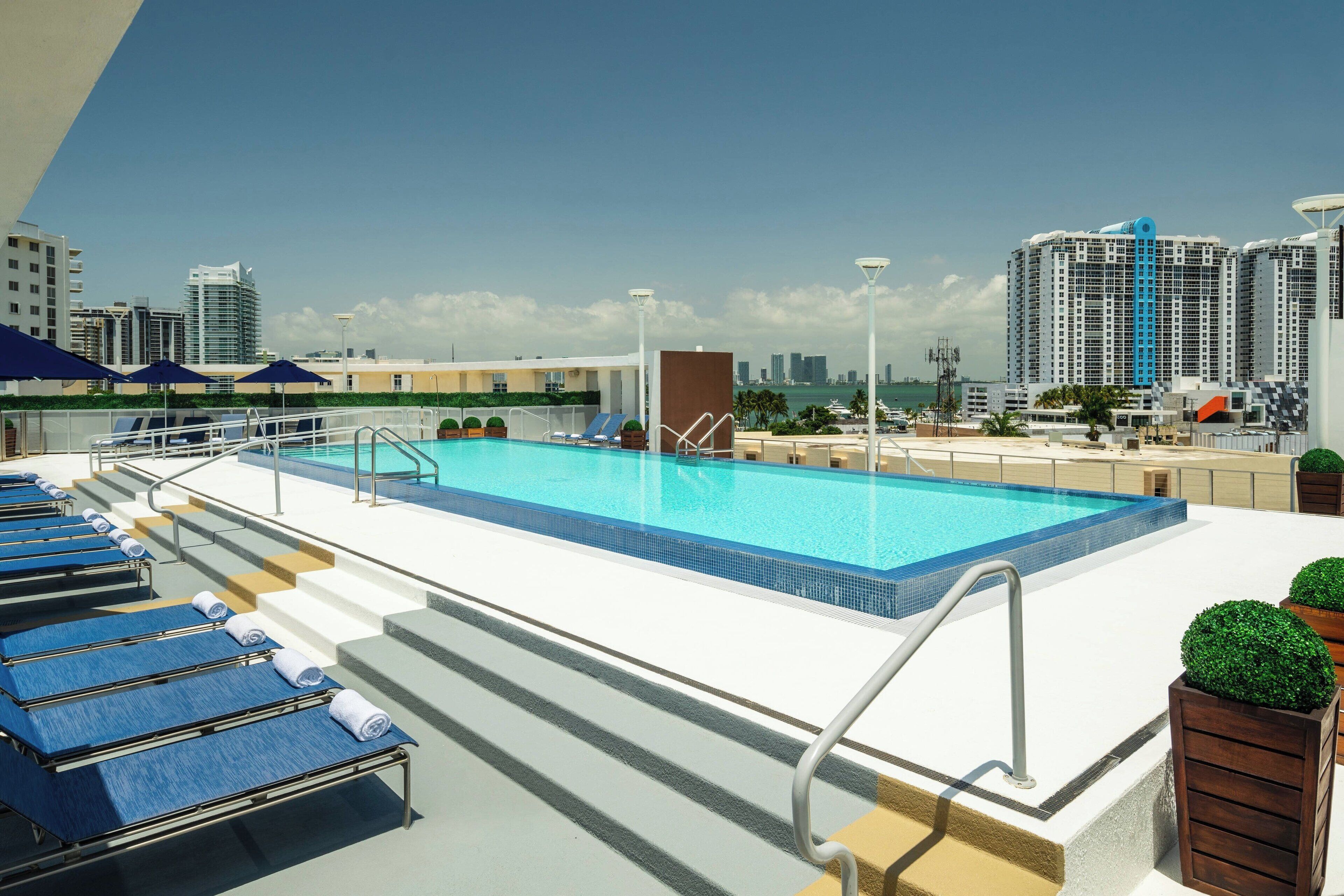 A rooftop pool with lounge chairs and a city skyline in the background.