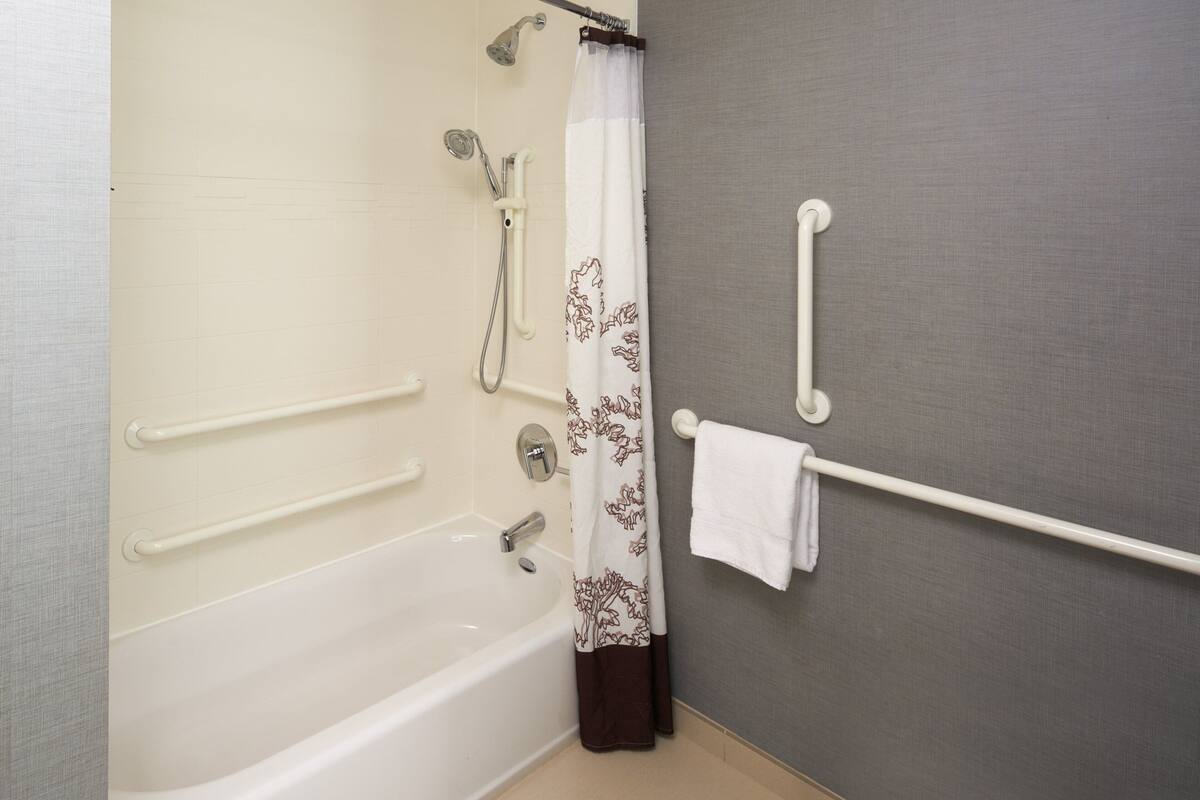 A bathroom with a bathtub, grab bars, a showerhead, and a towel rack.