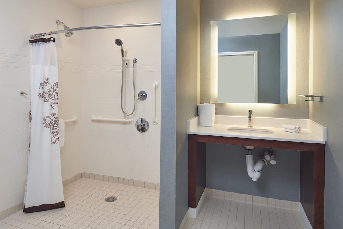 A bathroom with a shower, toilet, sink, and mirror.