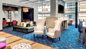 A spacious lobby with a blue patterned carpet, a grey sofa with red chairs, a fireplace, and a large TV mounted on the wall. - Residence Inn by Marriott Philadelphia Airport (Philadelphia)