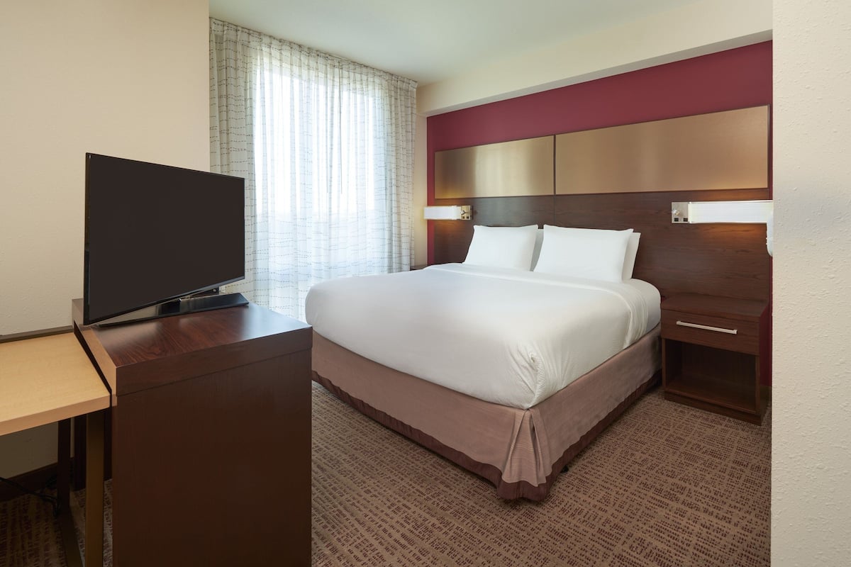 A hotel room with a bed, a TV on a desk, and a nightstand.