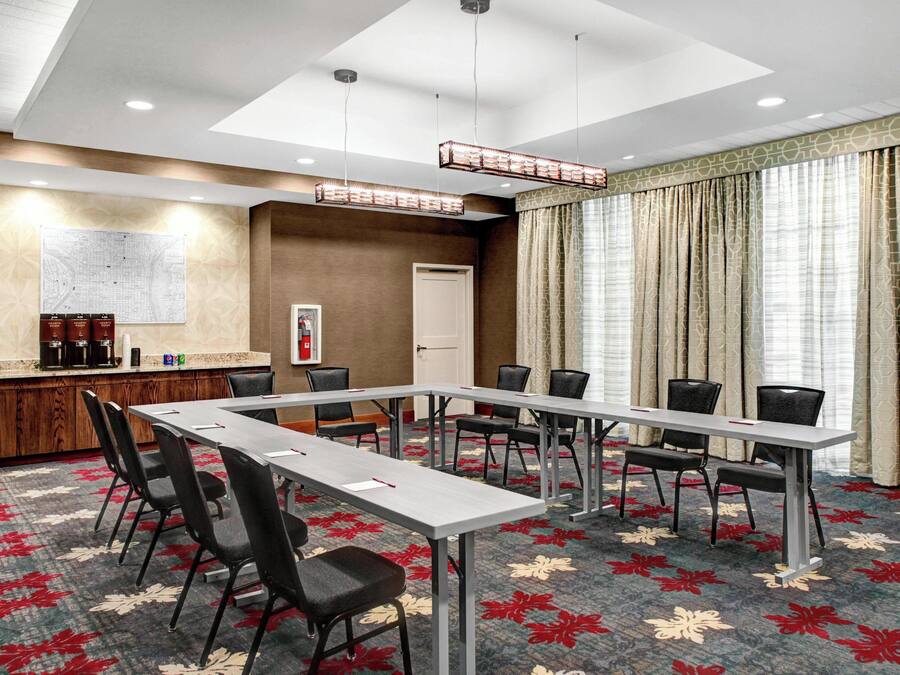 A conference room with a long table, chairs, a coffee station, a map on the wall, and a large window with curtains.