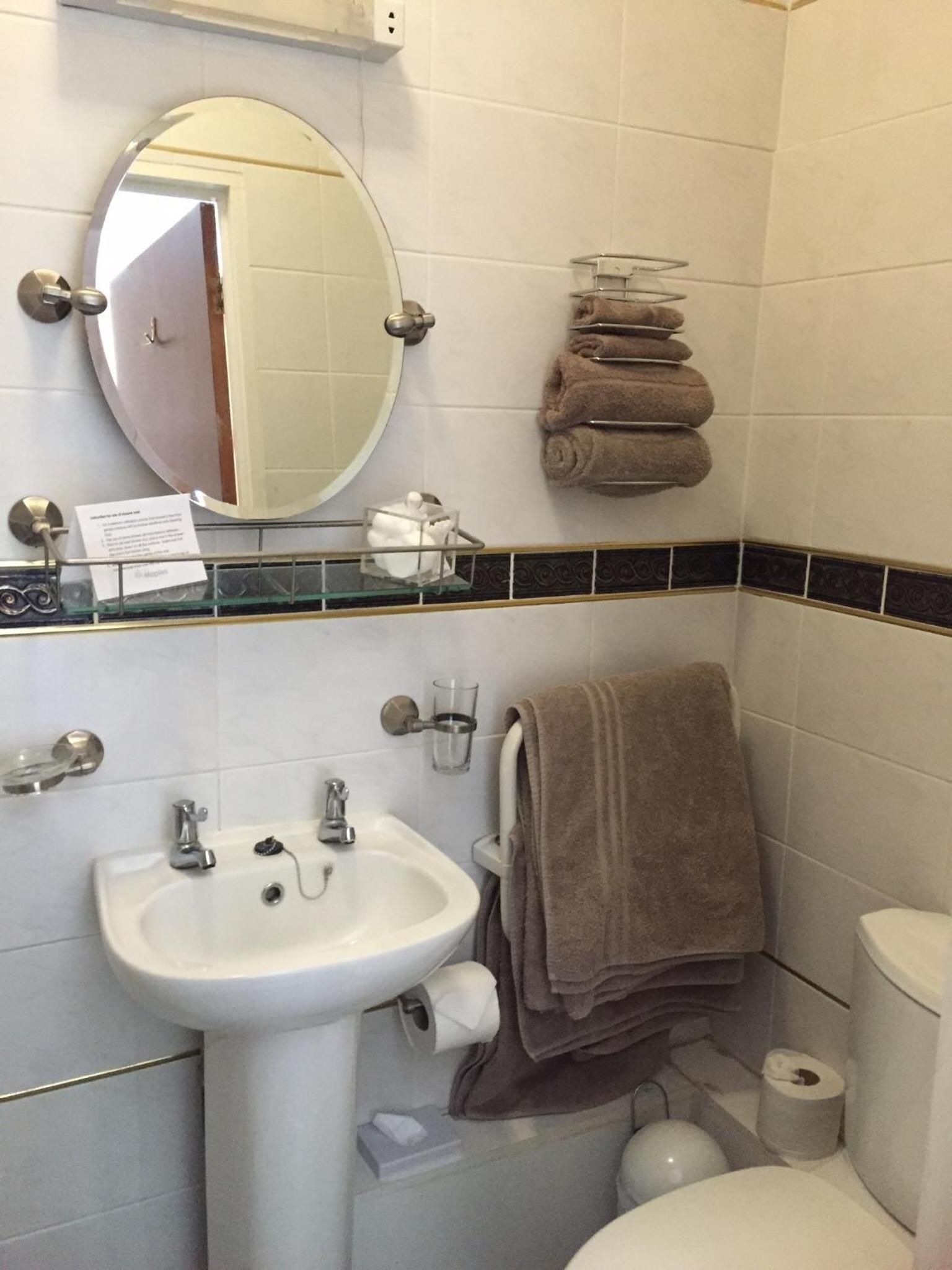 A bathroom with a white sink, a mirror, a toilet, and a towel rack with folded towels.