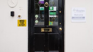 Une porte noire avec un panneau en verre, un heurtoir en laiton et une pancarte « Bienvenue » pour le Bed and Breakfast The Maples.