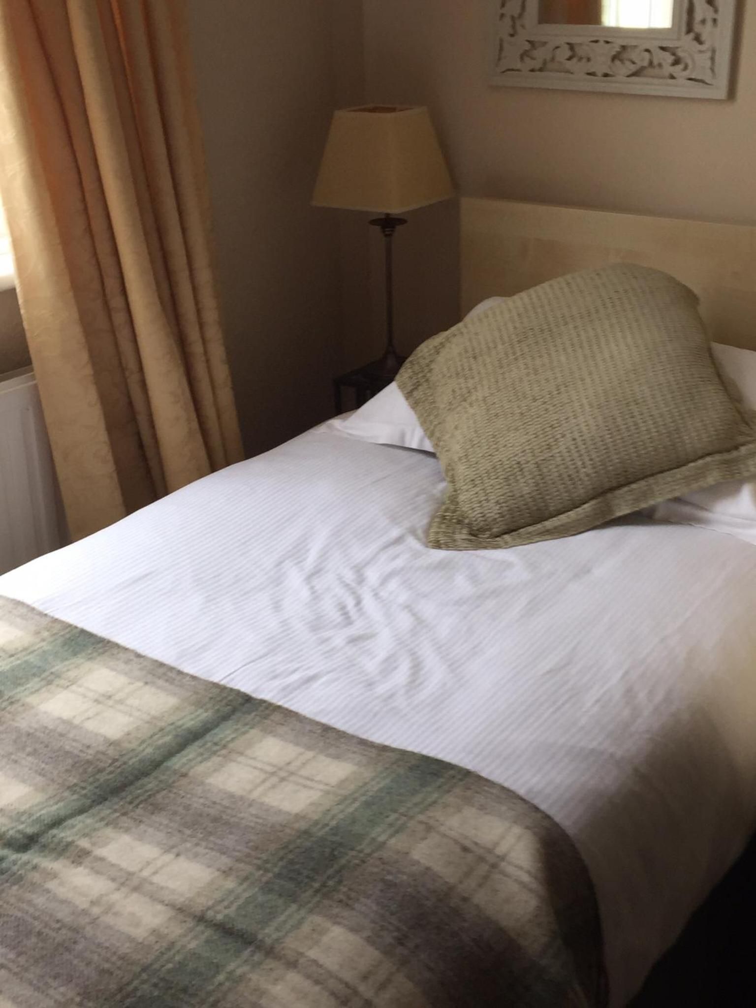 Una cama con sábana blanca, manta escocesa y una sola almohada.