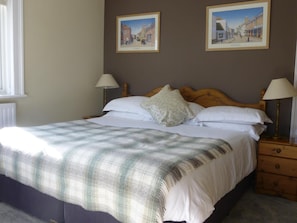 A neatly made bed with a plaid blanket, two bedside lamps, and two framed pictures on the wall. - The Maples (Southampton)