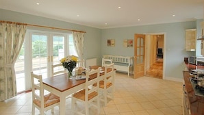 A dining area with a wooden table and chairs, a vase with flowers, and a view through large windows. - BCC Lochness Cottages (Inverness)