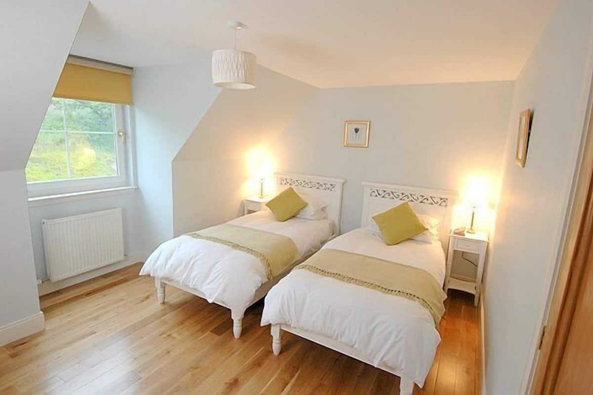 A bedroom with two beds, a window, a radiator, and a ceiling light.