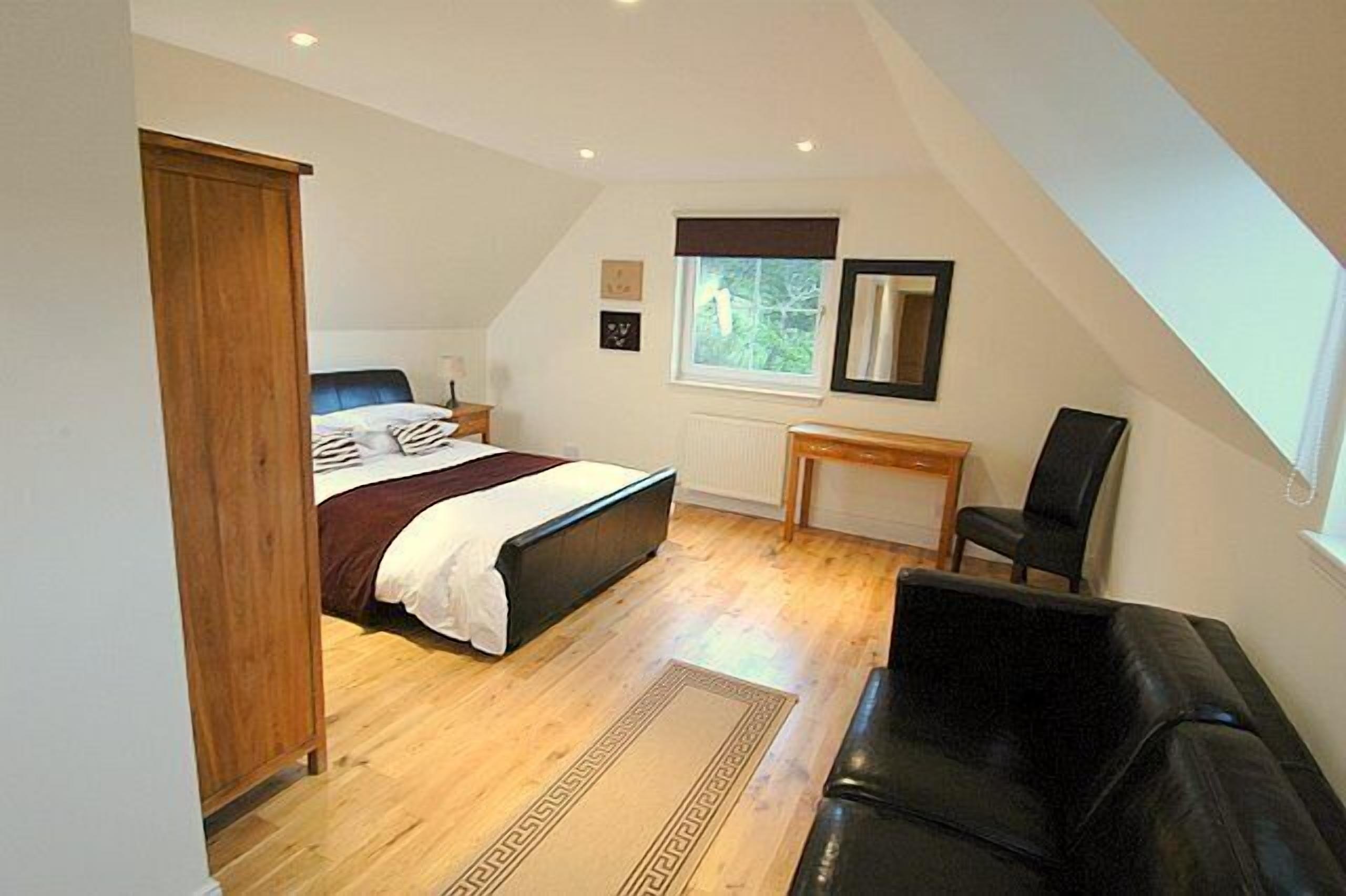 Een slaapkamer met een bed, een houten kledingkast, een bureau, een stoel en een raam.
