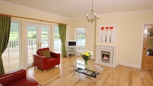 A spacious living room with a fireplace, a red sofa, a glass coffee table, and a television. - BCC Lochness Cottages (Inverness)