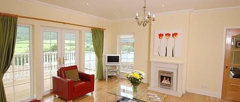 A spacious living room with a fireplace, a red sofa, a glass coffee table, and a television.