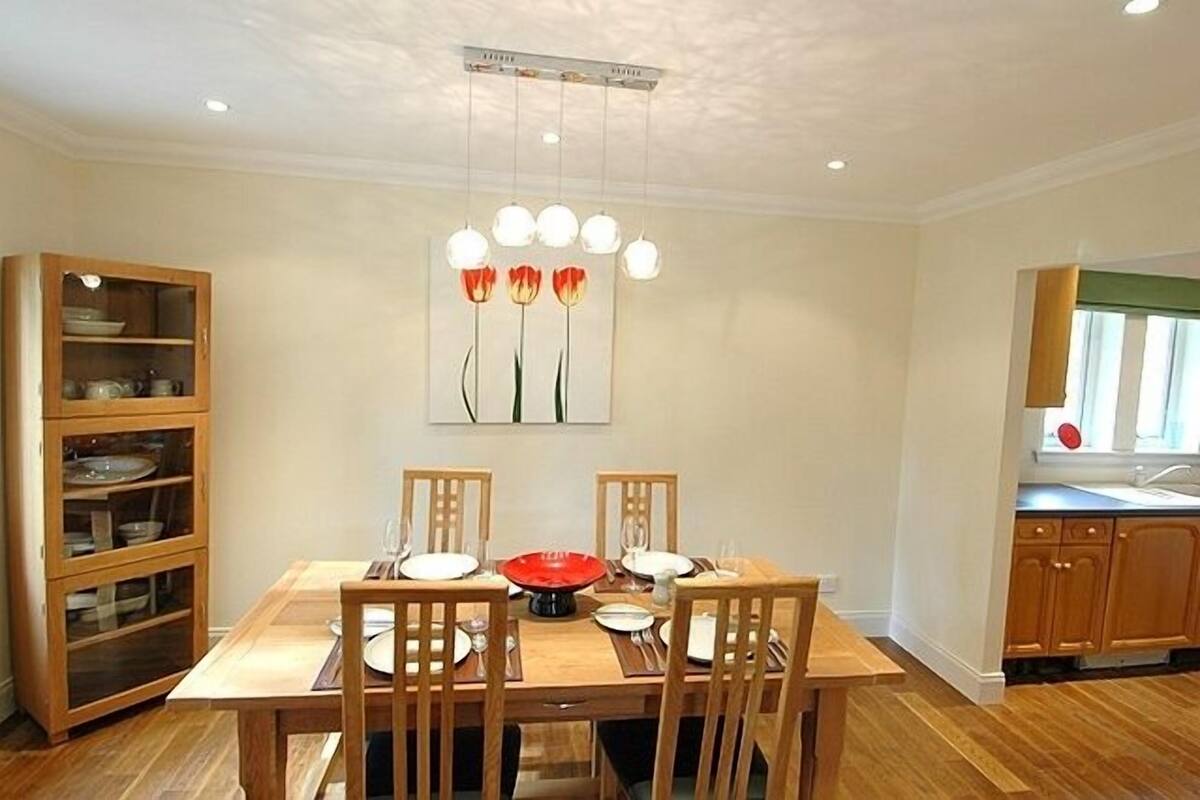 A dining area with a wooden table and chairs, a glass cabinet with dishes, and a painting of flowers on the wall.