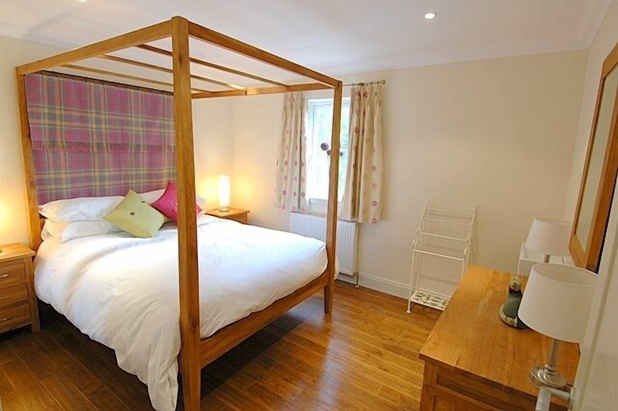 A four-poster bed with a plaid headboard, a bedside table with a lamp, and a wooden nightstand.