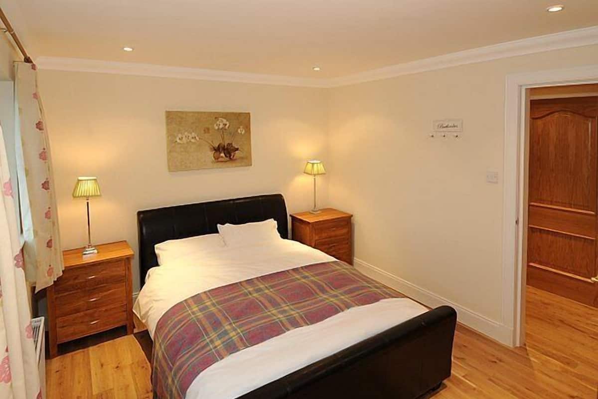 A bedroom with a bed, two bedside tables, a wooden floor, and a door.