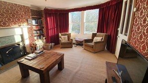 A living room with a fireplace, a bookshelf, two armchairs, a coffee table, and a television.