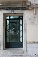 Une porte dotée d’un panneau en verre et d’un motif en forme de grille métallique, un panneau indiquant le numéro « 6 » au-dessus, et une enseigne sur le mur à droite.