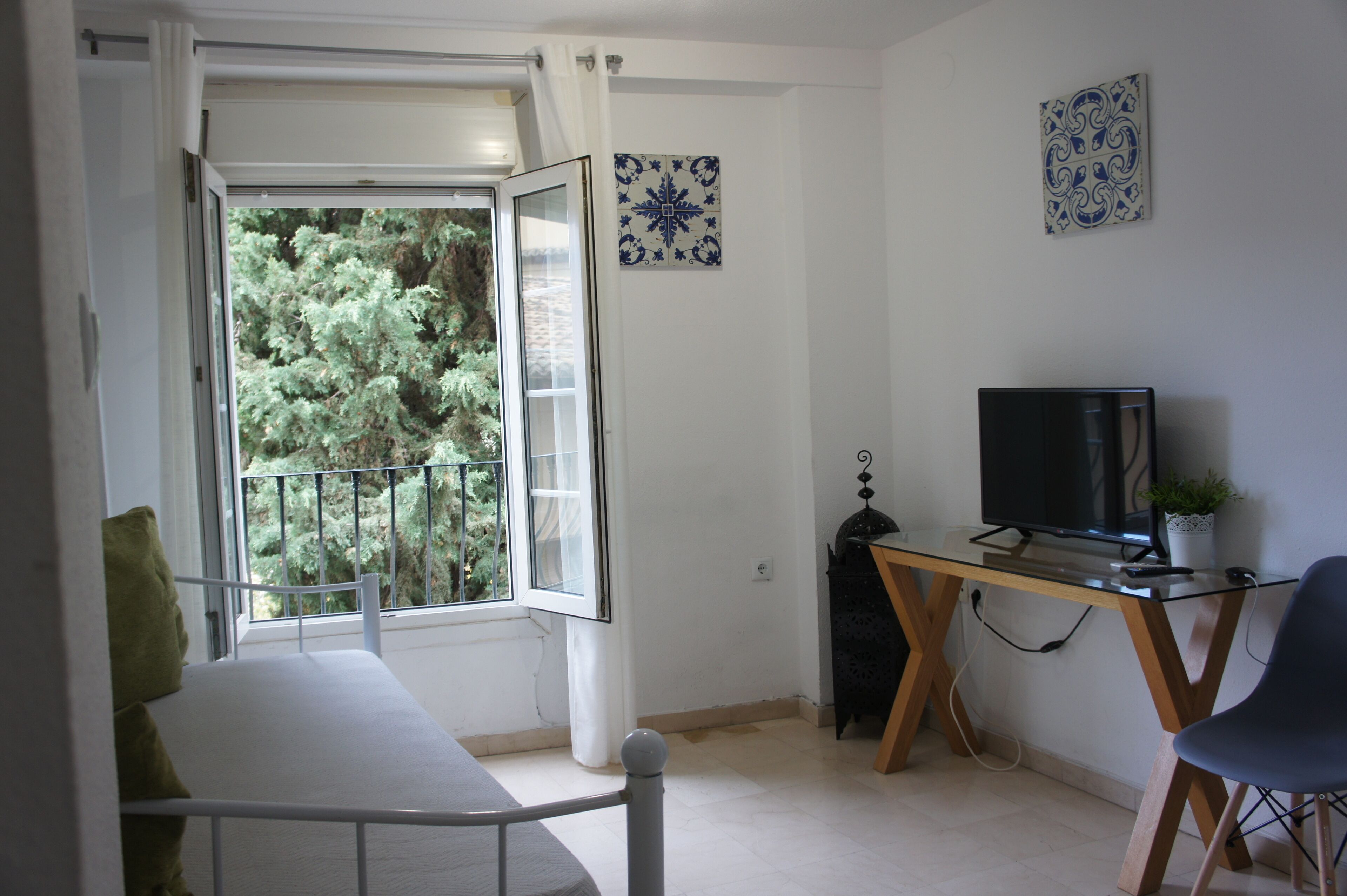 Una habitación con balcón, un escritorio con televisor y una silla.