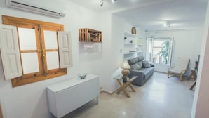 Una sala moderna con un sofá, una mesita de centro y una lámpara. Se ve una ventana con persianas de madera y un radiador en la pared.