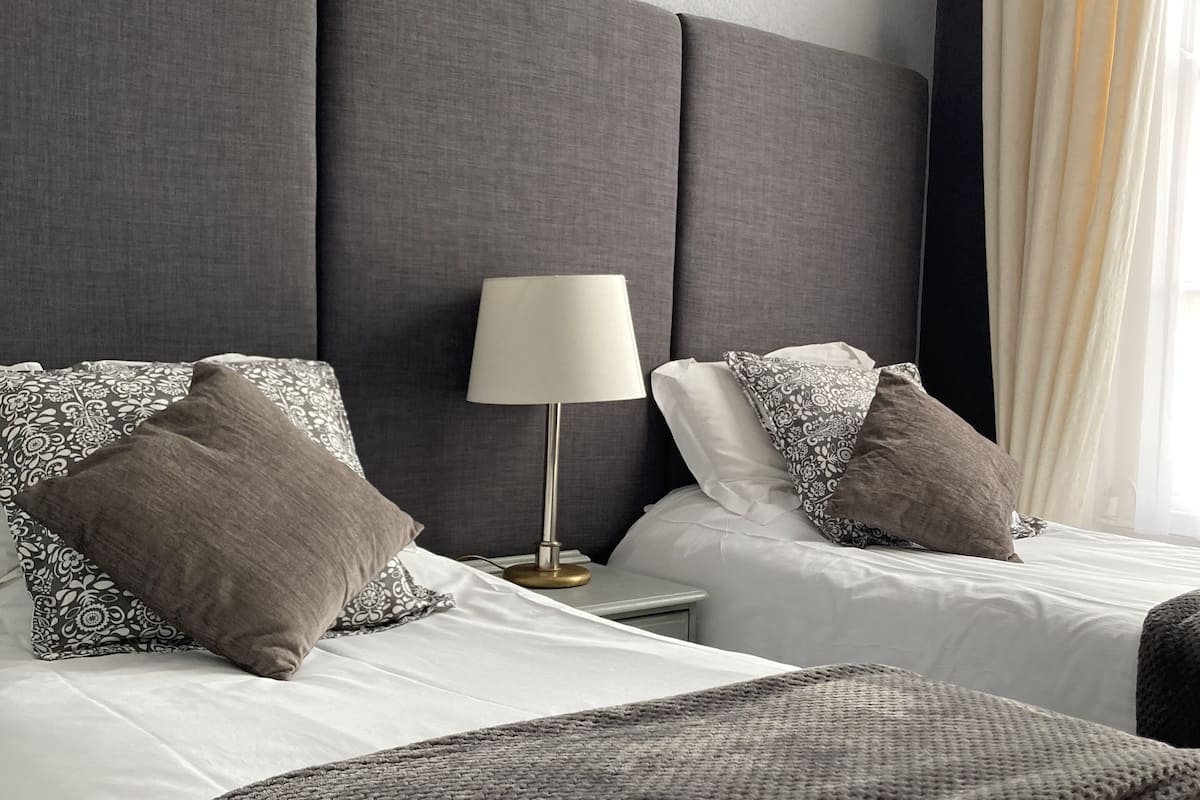 A hotel room with two beds, a bedside lamp, and a view of the outdoors.