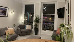 A living room with a grey sofa, a wooden coffee table, and a large window with a view of the city. - The Esplanade (Weymouth)