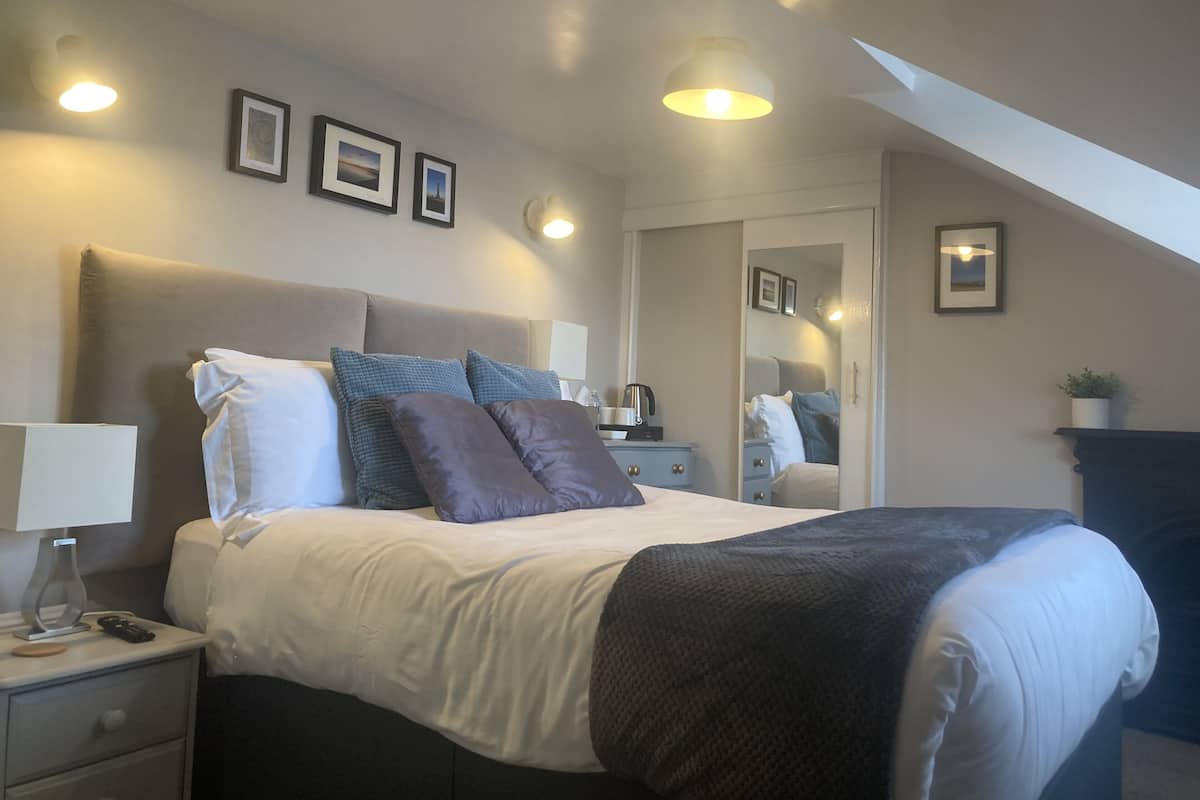 A neatly arranged bedroom with a bed, bedside tables, a mirror, and framed pictures on the wall.