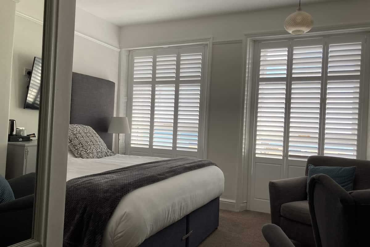 A bedroom with a bed, bedside tables, a chair, and large windows with blinds.