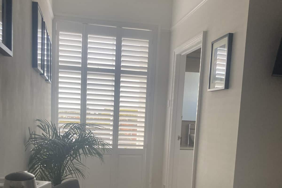 A compact living space with a dining area, a large window with blinds, a potted plant, and a bed.