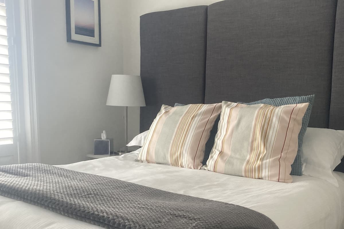 A neatly made bed with a grey headboard, white bedding, and striped pillows.