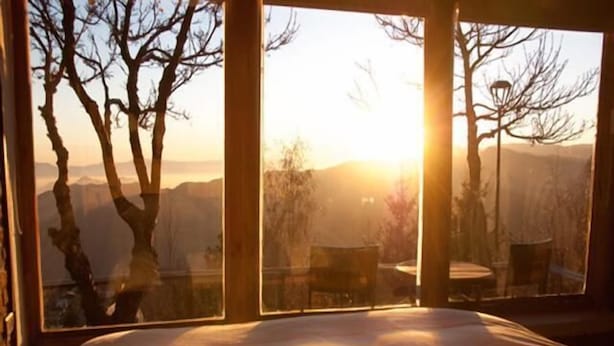 A bedroom with a large bed and a view of trees and mountains through open windows. - Lodge Cordillera (Lo Barnechea)