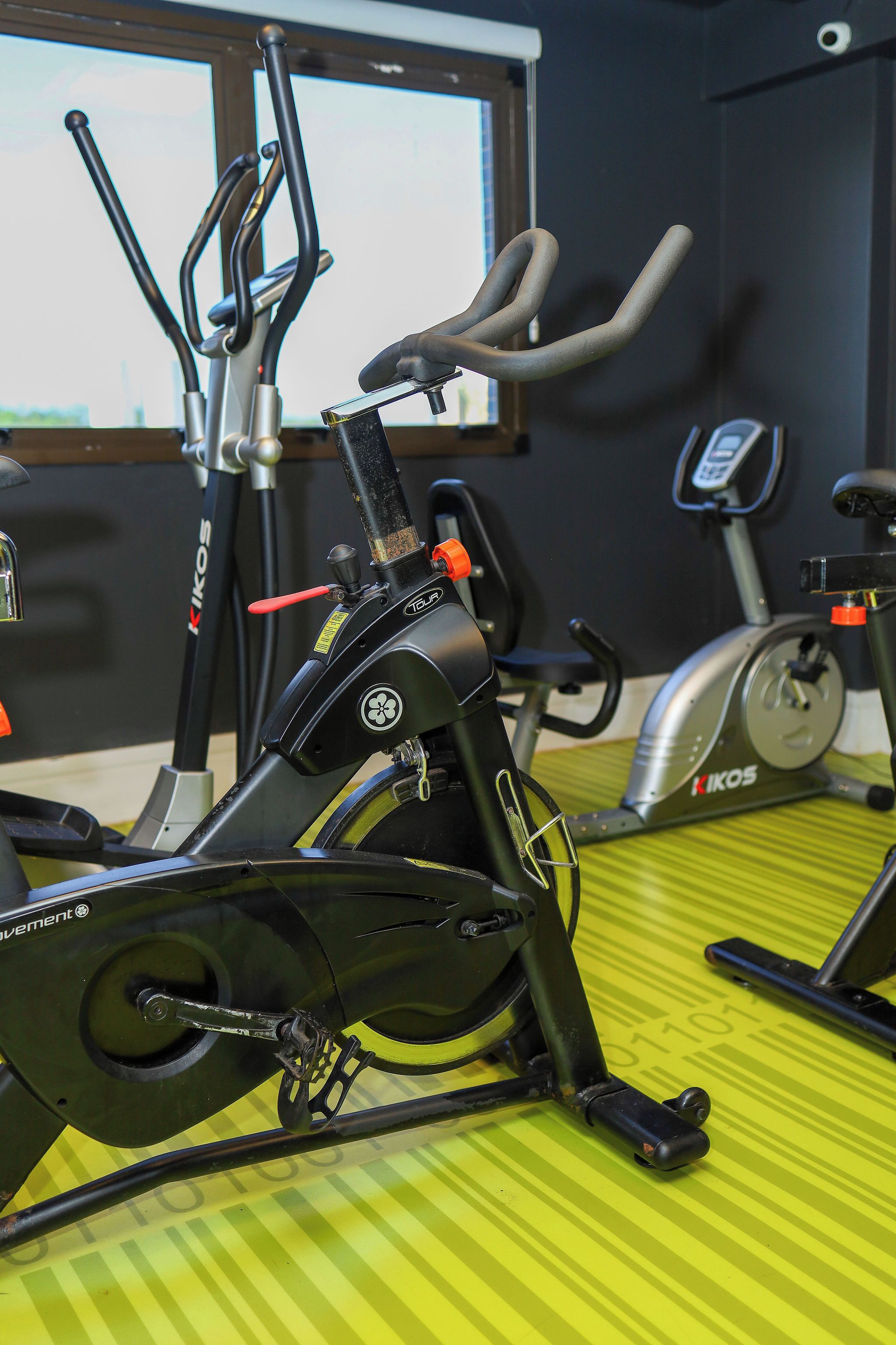 Ein stehendes Fahrrad mit einem digitalen Display, ein Fenster mit Blick und ein gelb gestreifter Boden.