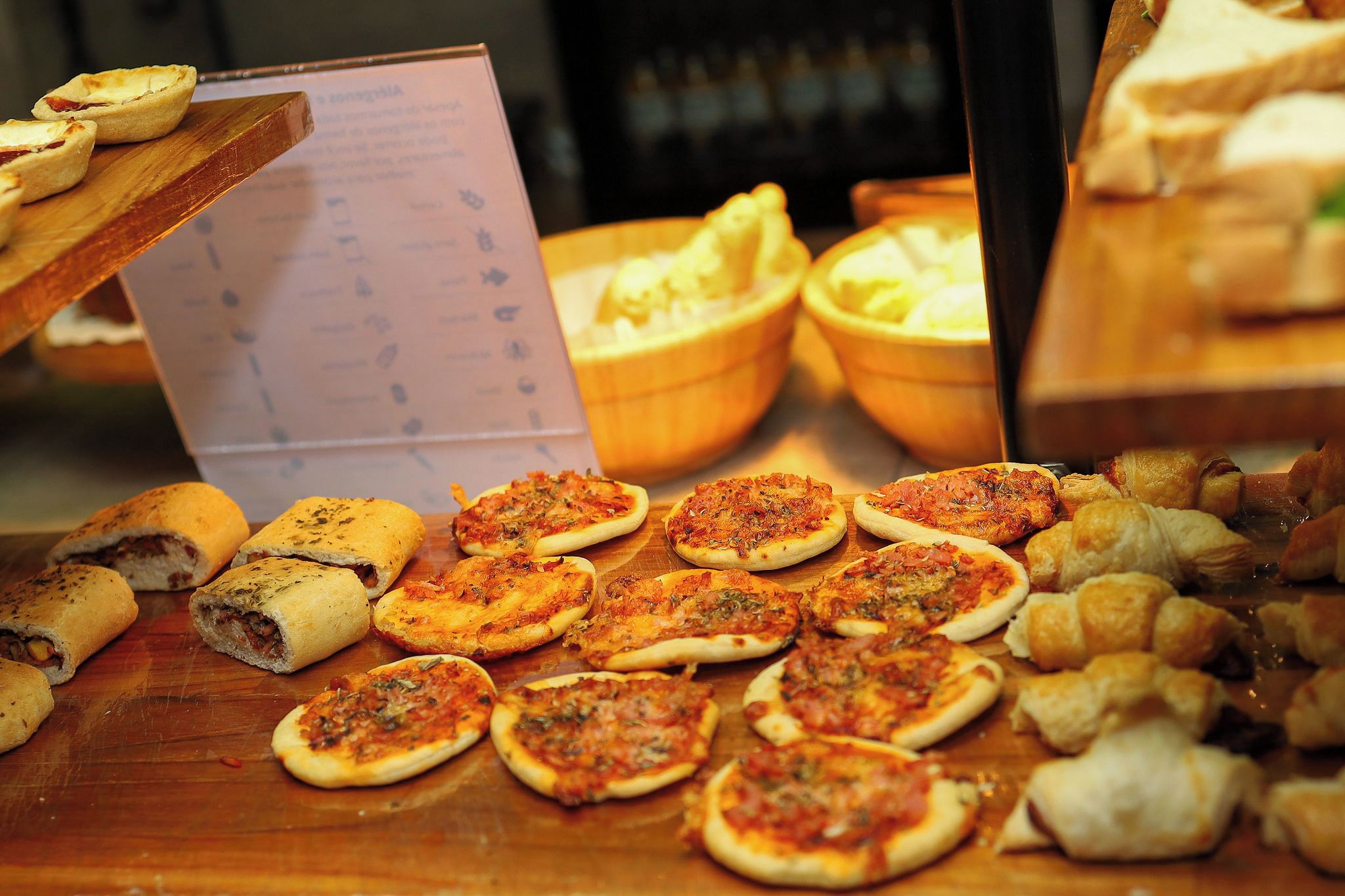 A variety of small pizzas and bread rolls displayed on a wooden table.