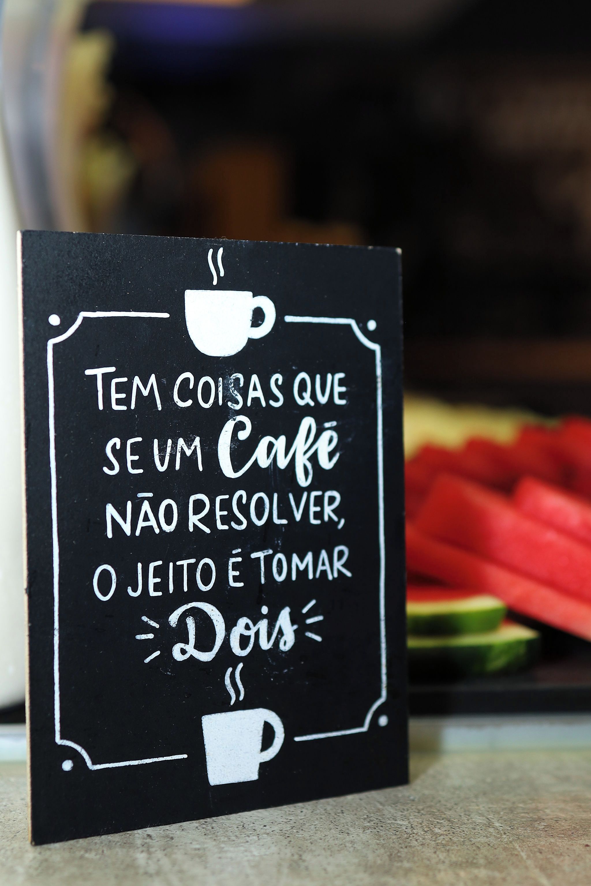 A black sign with white text and drawings of a coffee cup and steam, suggesting a café setting.