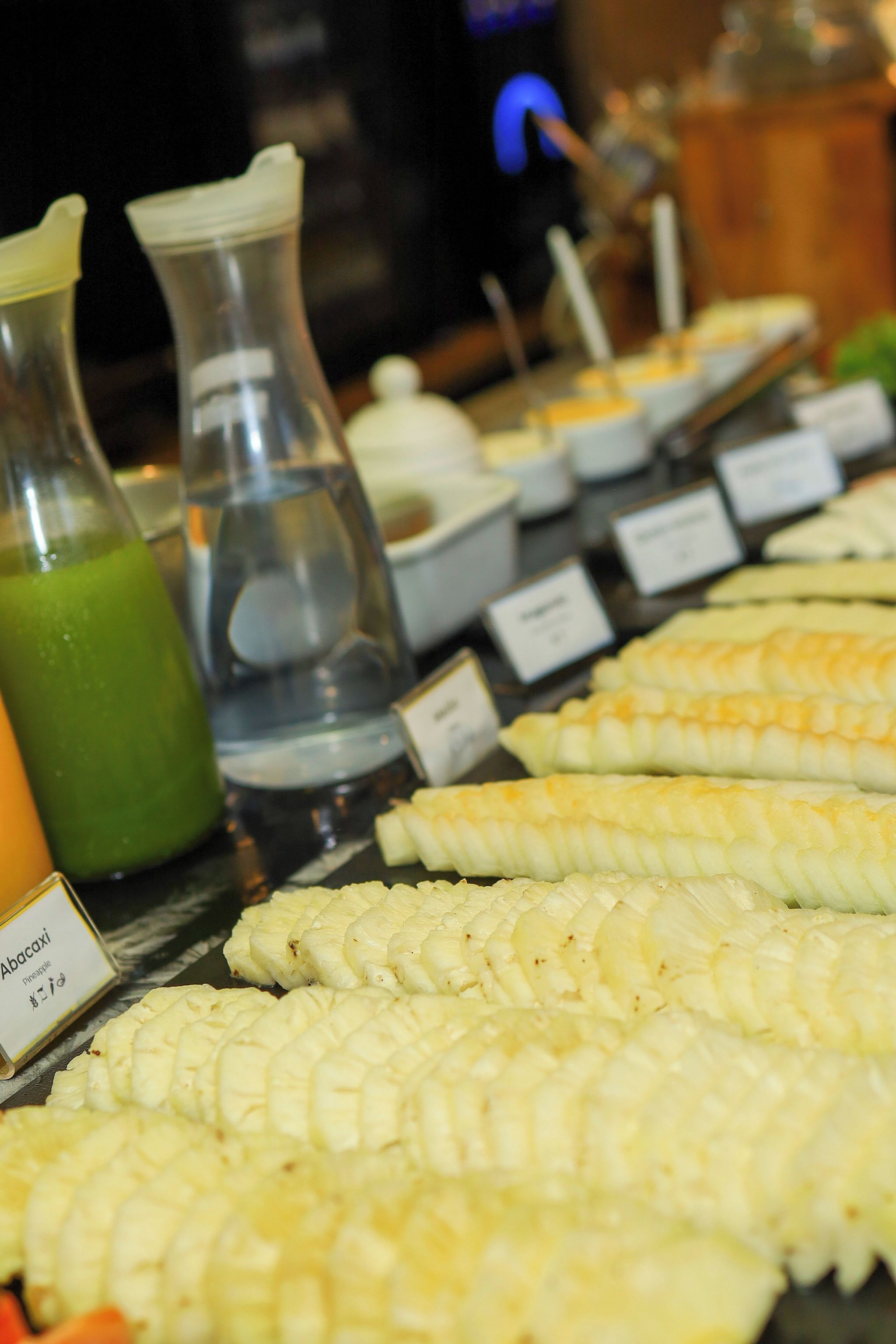 A buffet table with various food items, including corn on the cob and a green beverage.