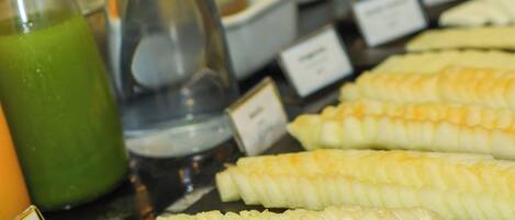 A buffet table with various food items, including corn on the cob and a green beverage.