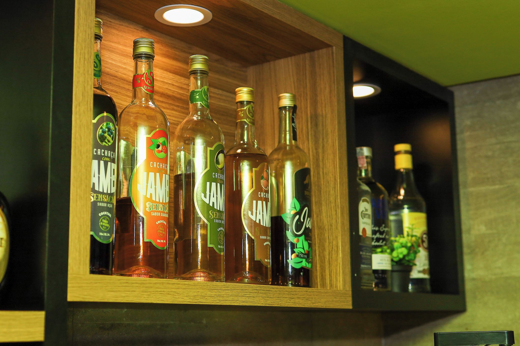 A wooden shelf with various bottles of alcohol, including JAMB and CACHACA.