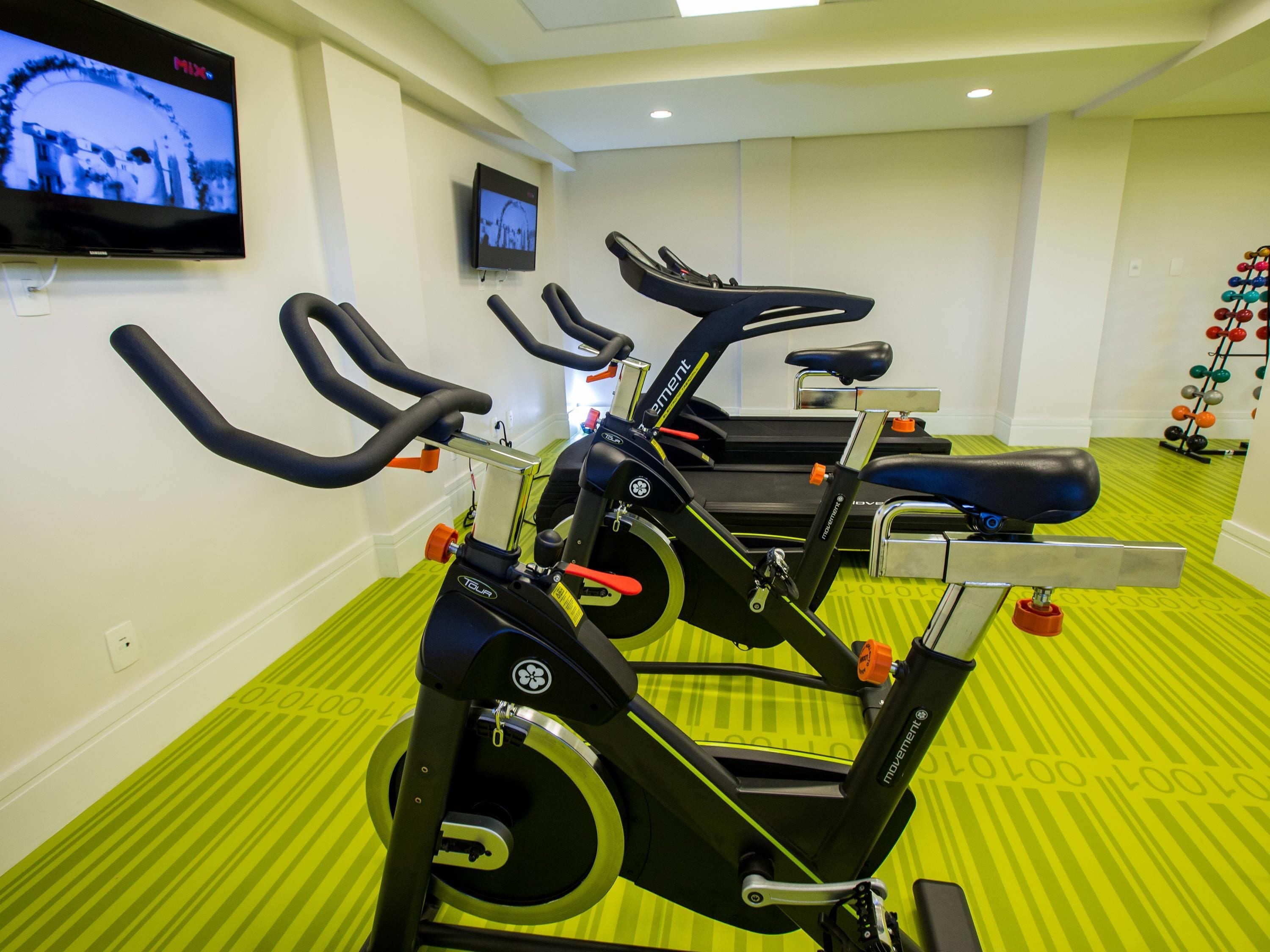 A gym with stationary bikes, a TV screen, and a wall-mounted TV.