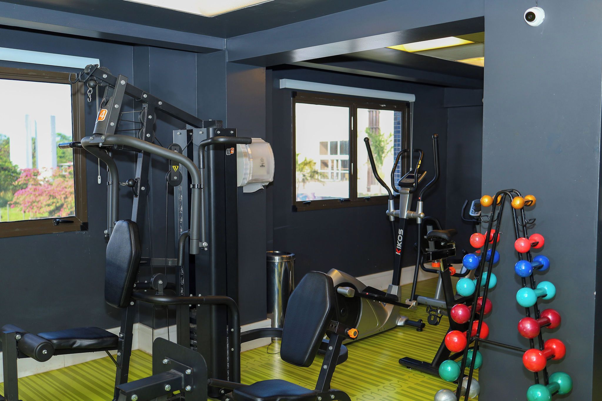 A gym with exercise equipment, a rowing machine, and a set of colorful dumbbells.