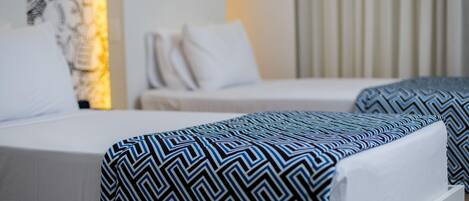 Habitación de hotel con dos camas, cada una con ropa de cama estampada, un ventanal con cortinas y una lámpara fijada a la pared.