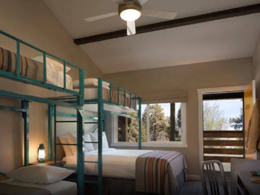 A bunk bed room with a ceiling fan, a window with a view of trees, and a desk with a chair.