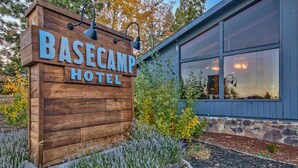 Een houten bordje van Basecamp Hotel, met een stenen muur en grote ramen.